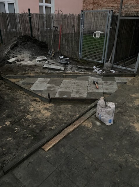 Układanie kostki brukowej w Łodzi: widok na częściowo ułożoną nawierzchnię, narzędzia pracy i materiały budowlane na placu budowy.