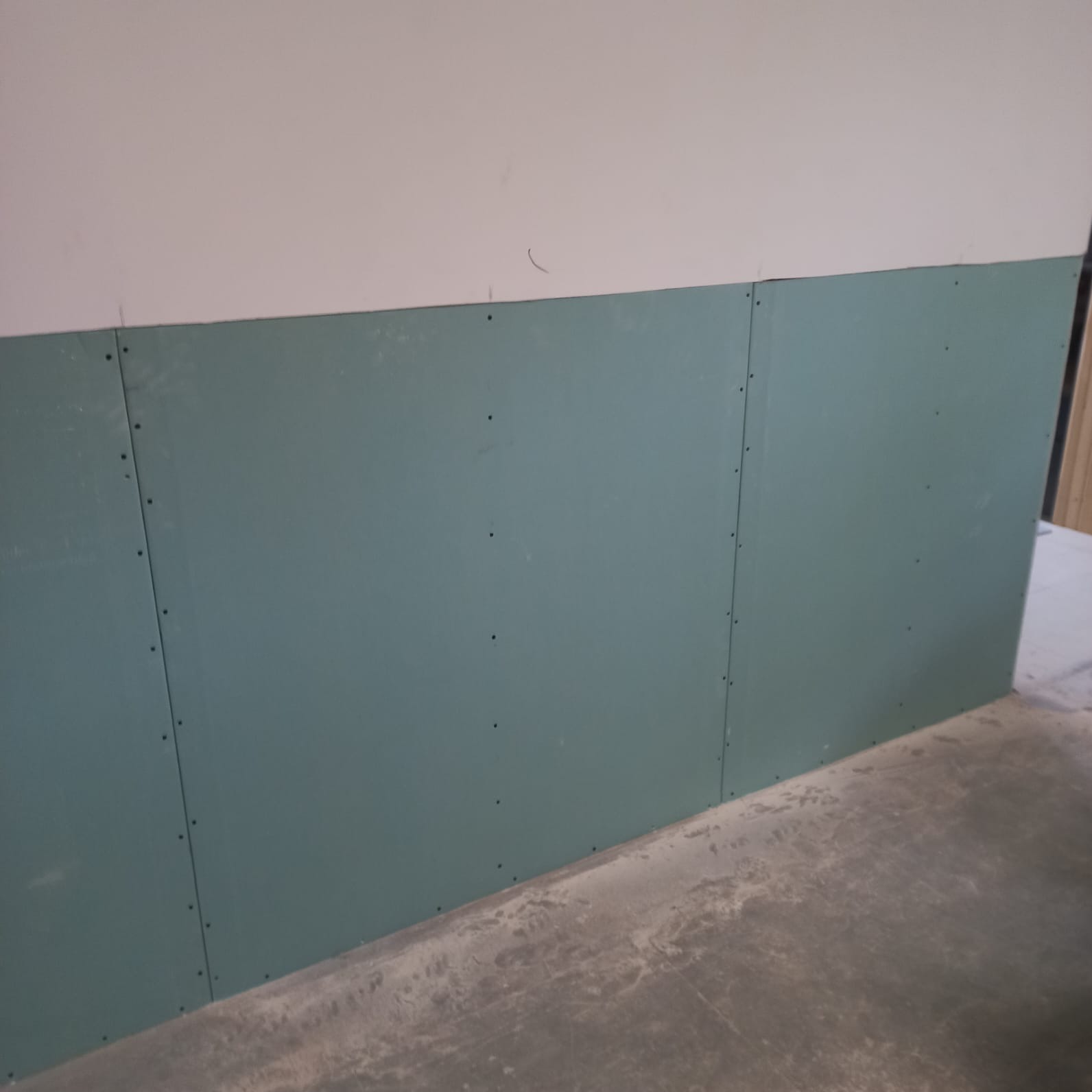 Świeżo zamontowane płyty gipsowo-kartonowe, przykręcone do ściany, widoczne szpachlowane łączenia między płytami.