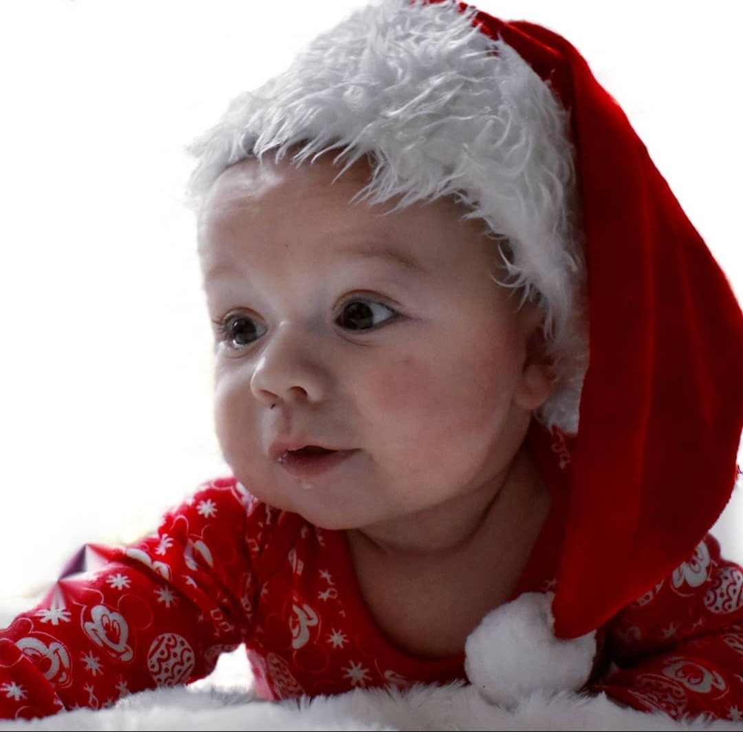 Niemowlę w czerwonym świątecznym stroju i czapce Mikołaja, leżące na białym futerku, sfotografowane w Wólce Okopskiej.
