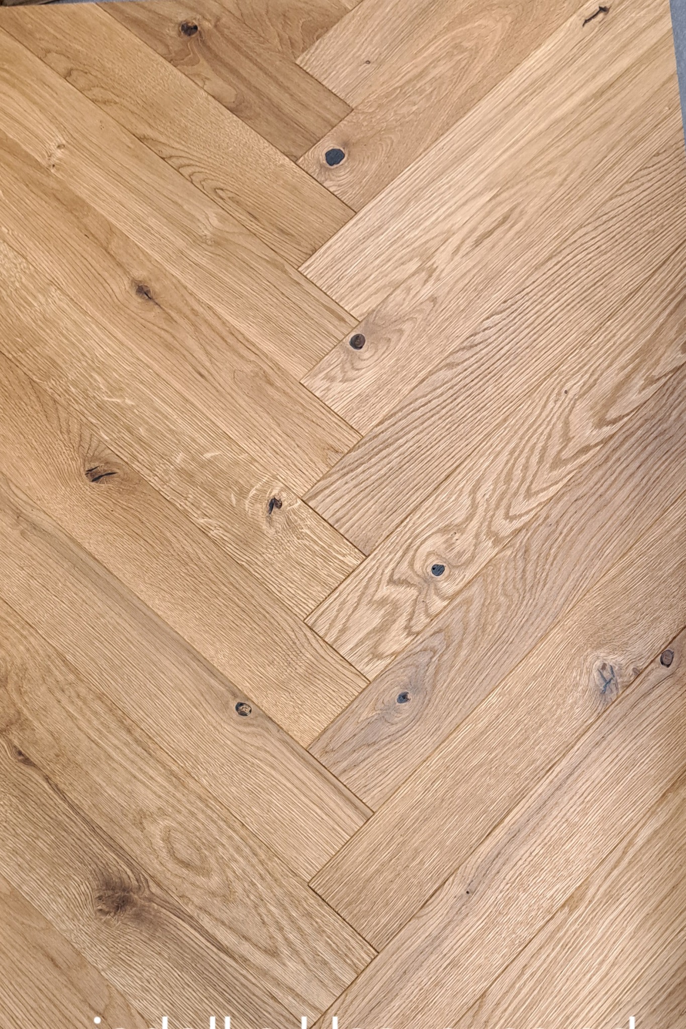 Ułożona w jodełkę jasna podłoga z drewnianych desek z wyraźnymi słojami i ciemnymi sękami.