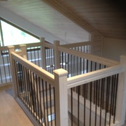 FIRMA STOLARSKO-CIESIELSKA PIOTR KUBIK - Jasna drewniana balustrada z czarnymi, metalowymi prętami, zabezpieczająca antresolę w domu z drewnianym sufitem i oknem dachowym.