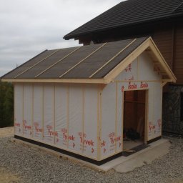 FIRMA STOLARSKO-CIESIELSKA PIOTR KUBIK - Konstrukcja szkieletowa budynku gospodarczego w trakcie budowy: drewniany szkielet obłożony membraną izolacyjną Tyvek i Isola, z dachem pokrytym papą, na podłożu z kamieni i betonowej wylewki,...