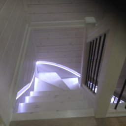 FIRMA STOLARSKO-CIESIELSKA PIOTR KUBIK - Drewniane schody spiralne z podświetleniem LED i czarnymi metalowymi balustradami, widok z góry.