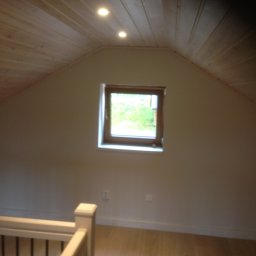 FIRMA STOLARSKO-CIESIELSKA PIOTR KUBIK - Poddasze z drewnianą boazerią na suficie, małe okno z widokiem na zieleń, fragment balustrady schodów.