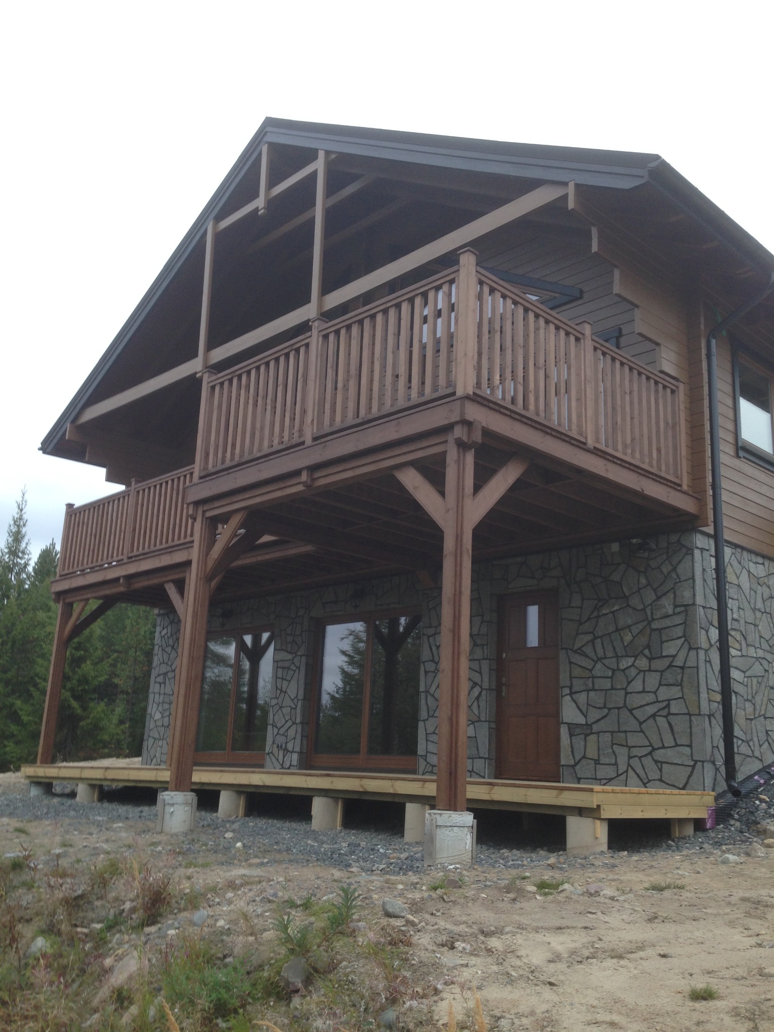 Dom z drewnianą konstrukcją balkonów wspartych na kamiennej elewacji, widok z dołu, surowy teren.