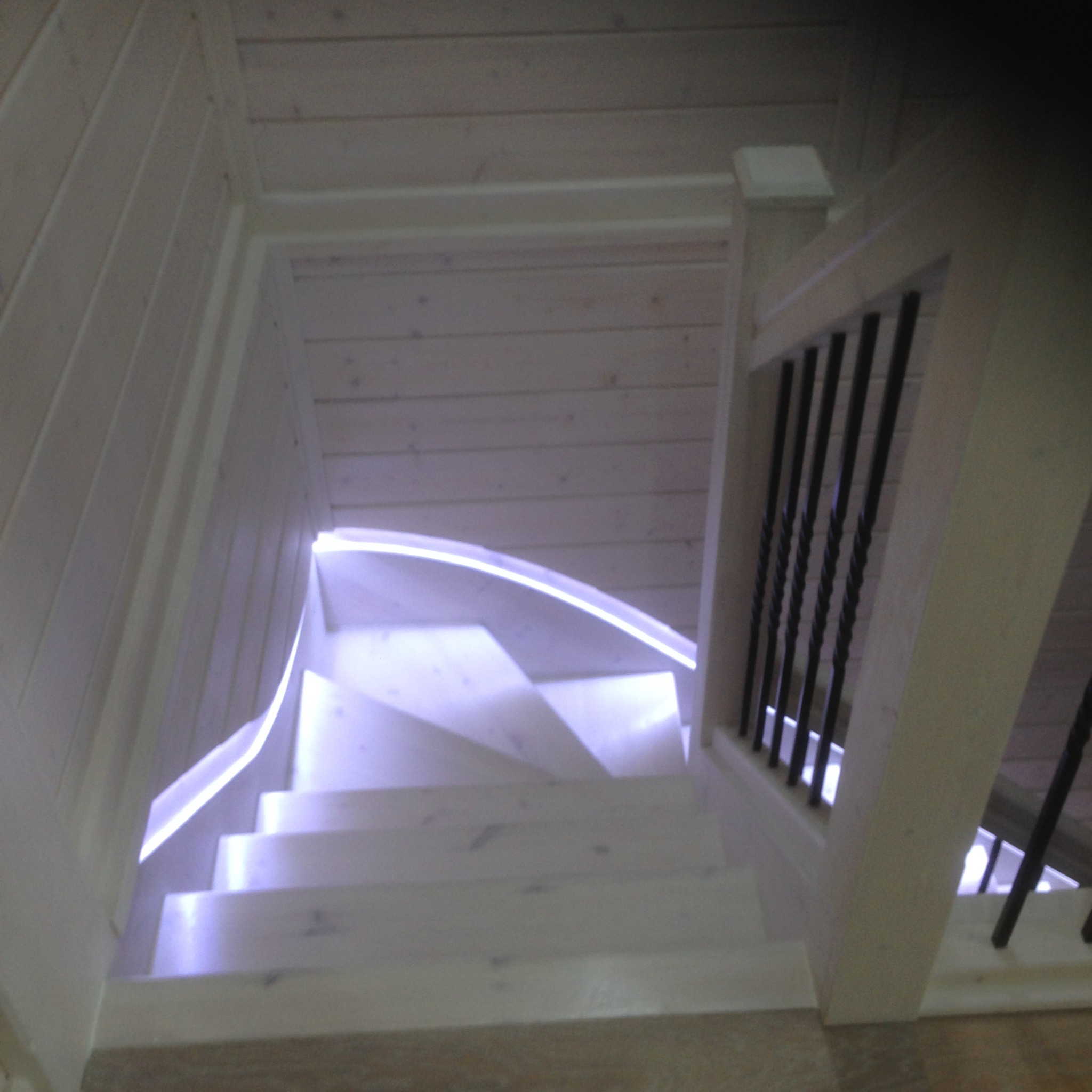 Drewniane schody spiralne z podświetleniem LED i czarnymi metalowymi balustradami, widok z góry.