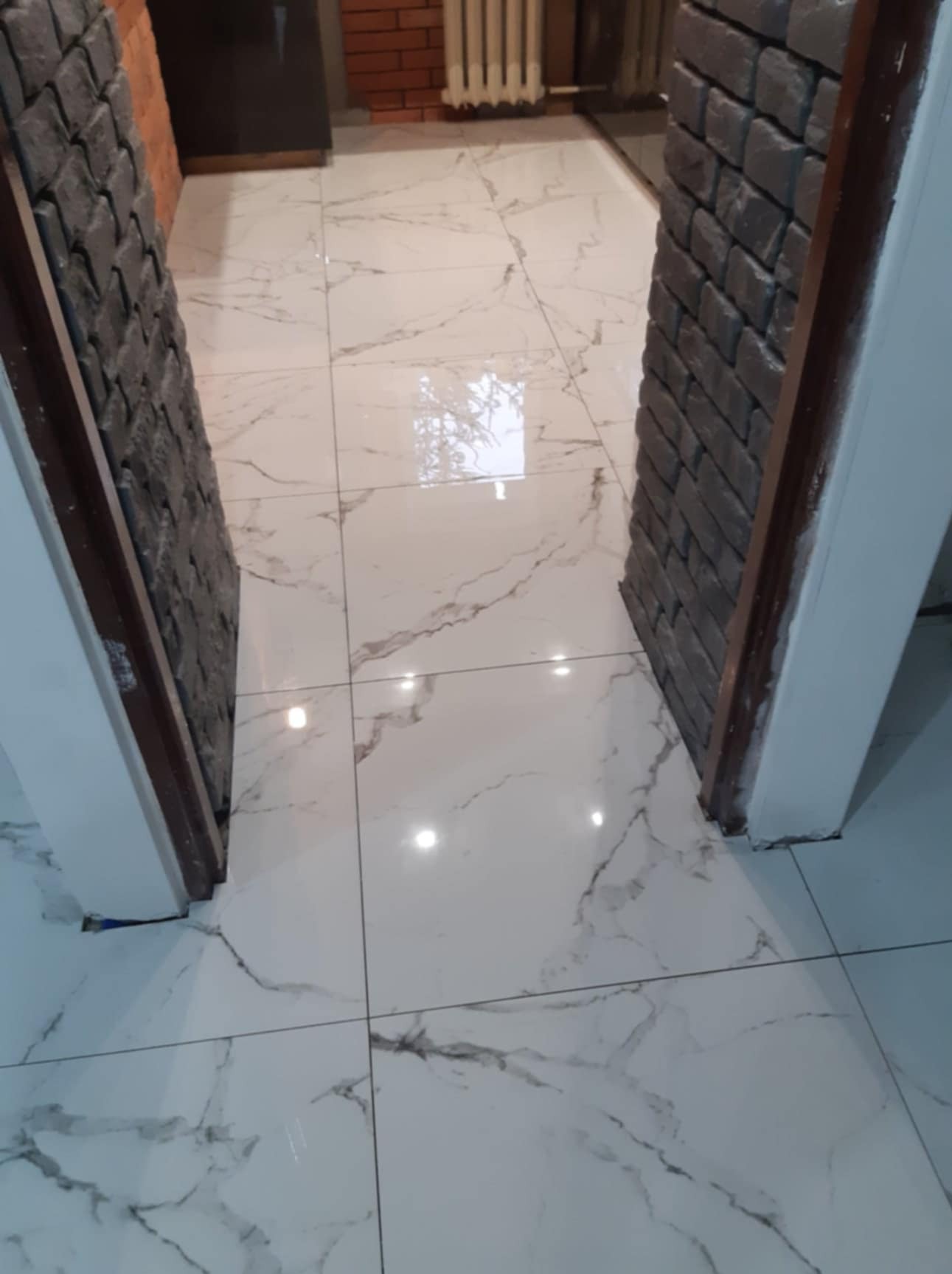 Wykończone wejście z białymi płytkami imitującymi marmur i dekoracyjną okładziną z szarej cegły na ścianach.