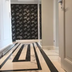 Wnętrze korytarza z marmurową podłogą w geometryczne wzory, ściana w czarno-srebrną tapetę z motywem jaszczurek, oświetlenie sufitowe punktowe.