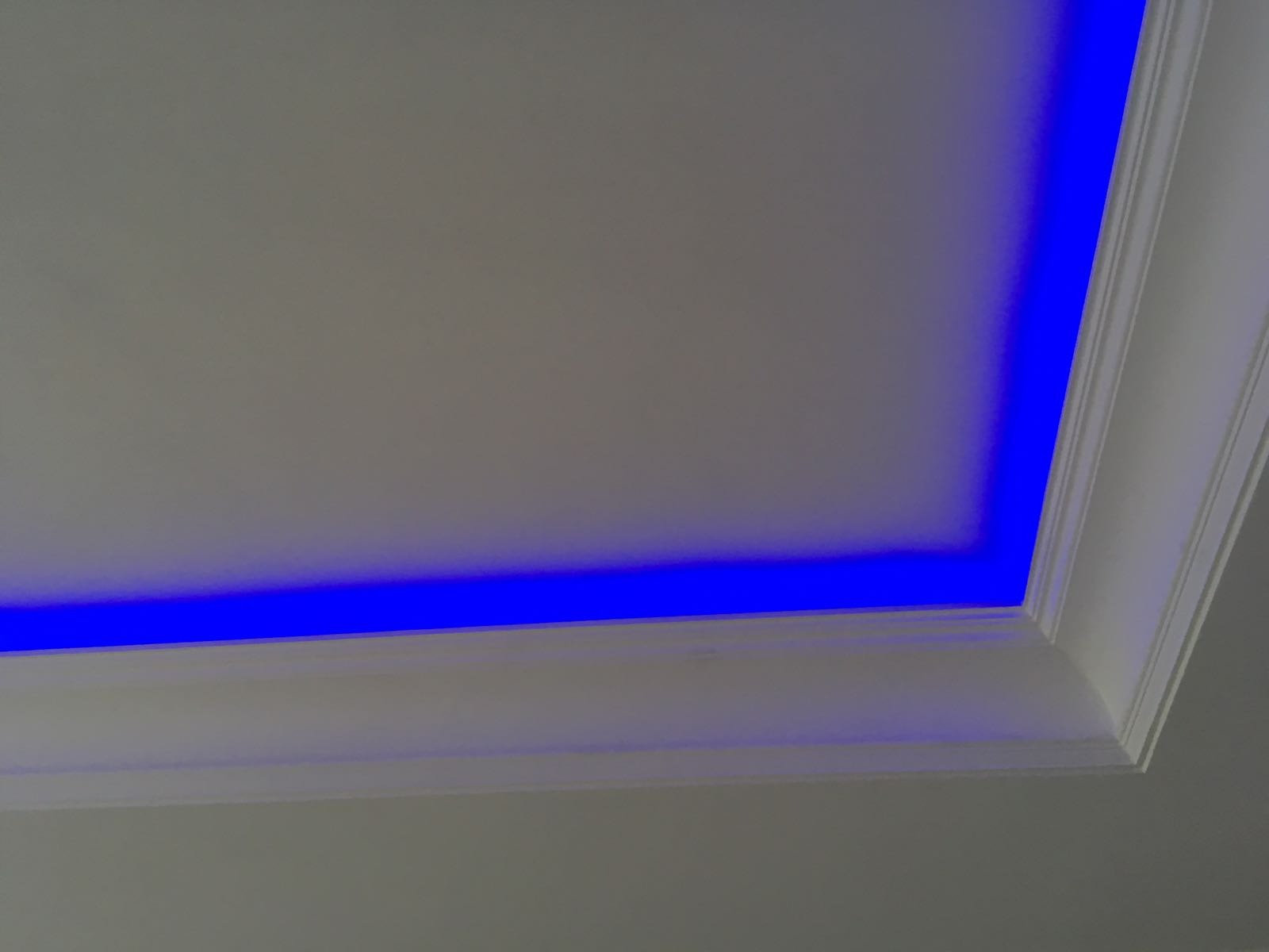 Fragment sufitu z oświetleniem LED w kolorze niebieskim, listwa dekoracyjna przy krawędzi.