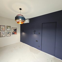 EKONEX SPÓŁKA Z OGRANICZONĄ ODPOWIEDZIALNOŚCIĄ - Pokój po malowaniu ścian na dwa kolory: jasny beż i granat, z widocznymi puszkami elektrycznymi, nowoczesną lampą wiszącą i klimatyzatorem.