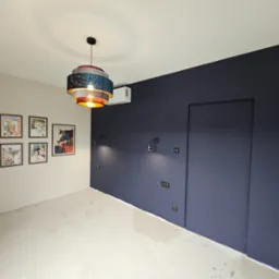 Pokój po malowaniu ścian na dwa kolory: jasny beż i granat, z widocznymi puszkami elektrycznymi, nowoczesną lampą wiszącą i klimatyzatorem.