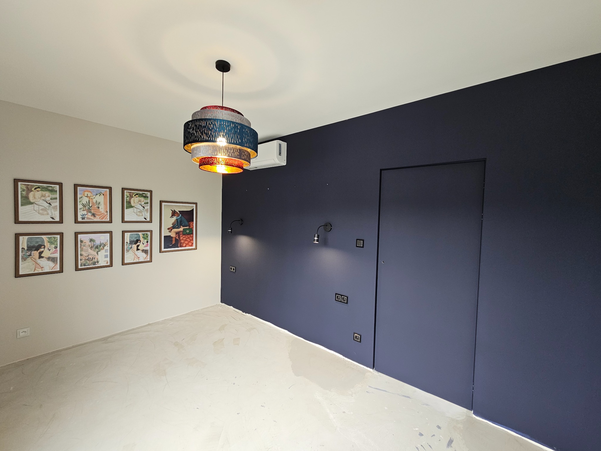 Pokój po malowaniu ścian na dwa kolory: jasny beż i granat, z widocznymi puszkami elektrycznymi, nowoczesną lampą wiszącą i klimatyzatorem.