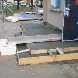 Roboty ogólno budowlane - Wylewanie betonowych schodów wejściowych do budynku, szalunek z desek, widoczne materiały izolacyjne i płyty.