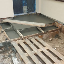 Roboty ogólno budowlane - Wylewka betonowa na tarasie w trakcie wykonywania, widoczne drewniane szalunki i paleta, okno zabezpieczone folią.