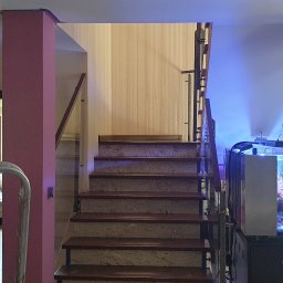 Roboty ogólno budowlane - Wnętrze domu w trakcie odświeżania, widoczne schody z marmurowymi stopniami, kolumny pomalowane na różowo, drabina malarska w tle oraz akwarium z oświetleniem LED.