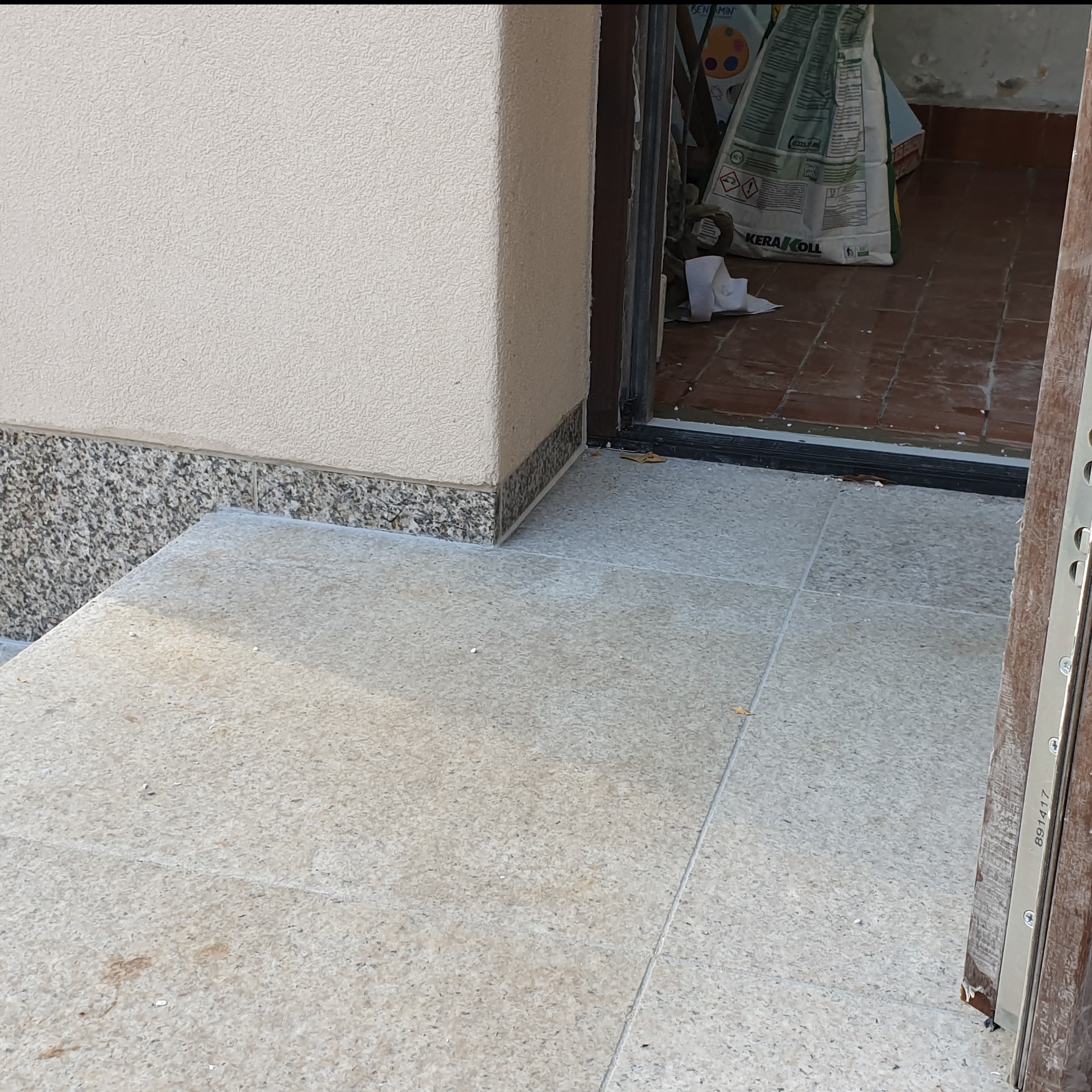 Wykończone płytki na schodach wejściowych, z fragmentem elewacji i workiem zaprawy w tle, widoczne z bliska.