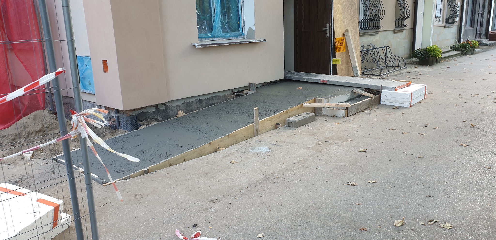 Betonowy podjazd dla niepełnosprawnych w trakcie budowy przed budynkiem w Pruchniku, widoczne drewniane szalunki i świeży beton.