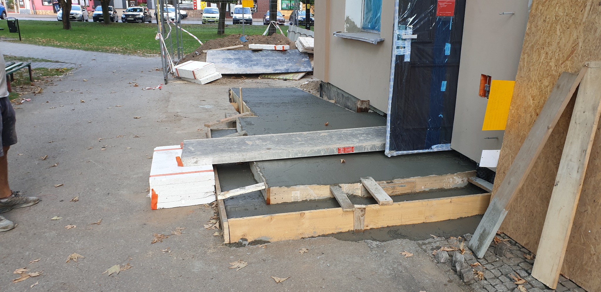 Wylewanie betonowych schodów wejściowych do budynku, szalunek z desek, widoczne materiały izolacyjne i płyty.