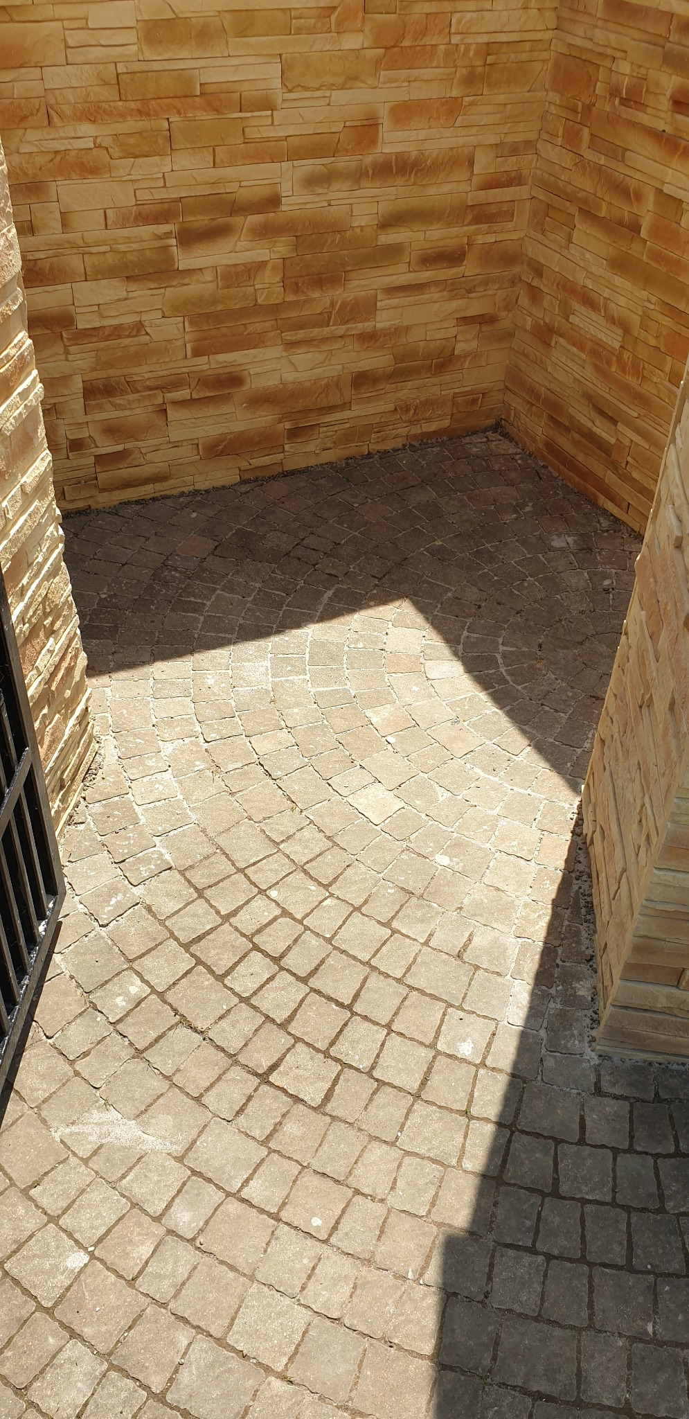 Wyłożony kostką brukową dziedziniec z dekoracyjną ścianą z kamienia elewacyjnego, oświetlony kontrastowym światłem słonecznym