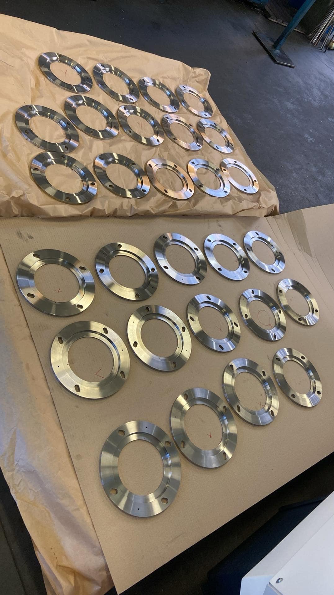 Partia obrobionych CNC, metalowych pierścieni kołnierzowych z otworami na śruby, ułożonych na papierze pakowym w hali produkcyjnej.