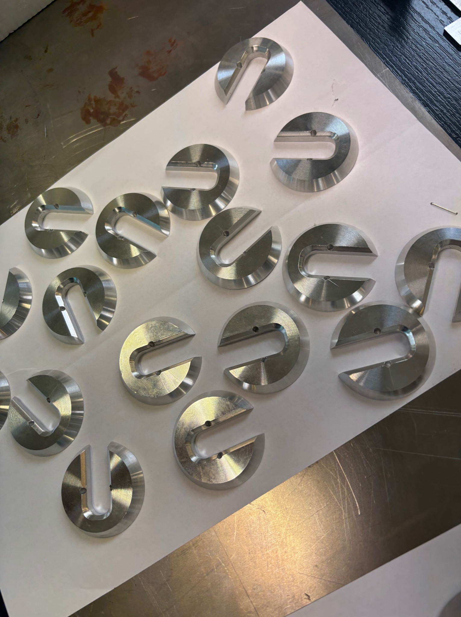 Partie identycznych, metalowych elementów w kształcie litery 'C' z otworem, ułożonych na białym papierze po obróbce.