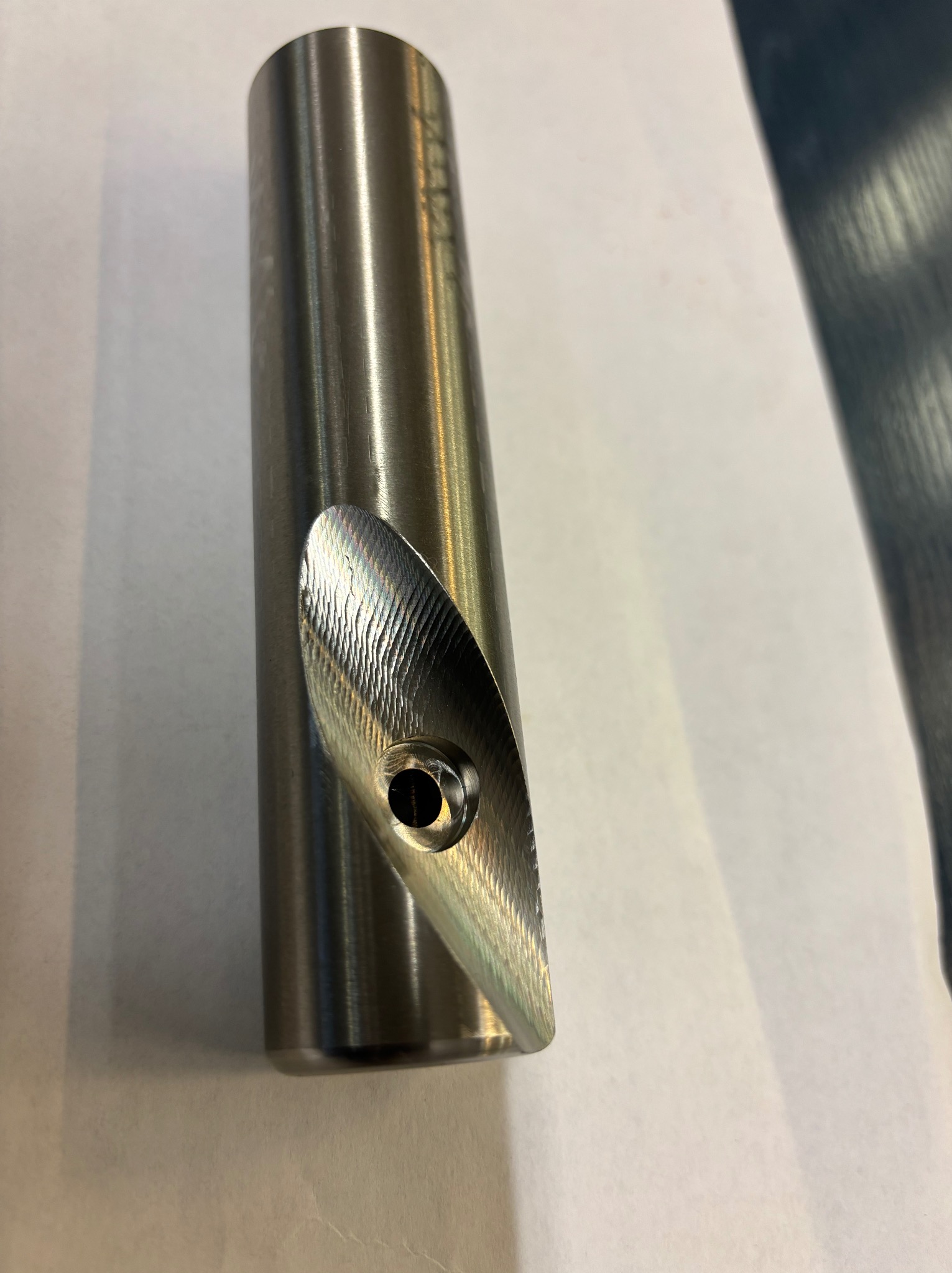 Metalowy cylinder z wyfrezowanym otworem i ukośną powierzchnią z widocznymi śladami obróbki, ukazujący precyzję wykonania.