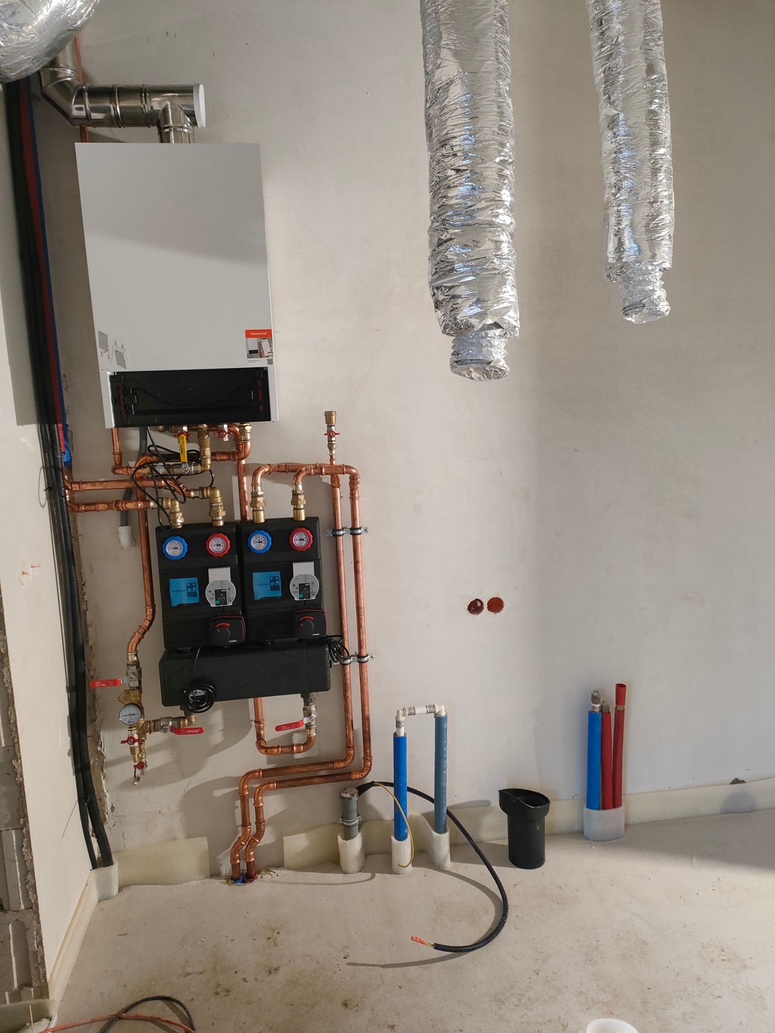 Nowoczesny piec grzewczy z miedzianą instalacją, czarnym rozdzielaczem z manometrami i przewodami wentylacyjnymi w surowym wnętrzu.