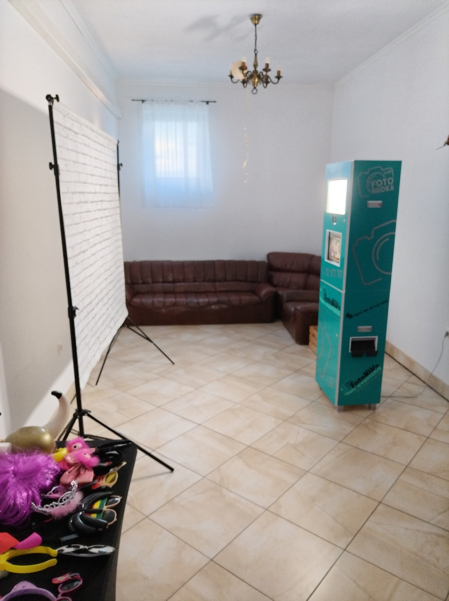 Wnętrze z ustawioną turkusową maszyną do robienia zdjęć, rekwizytami na stole i tłem imitującym cegły.