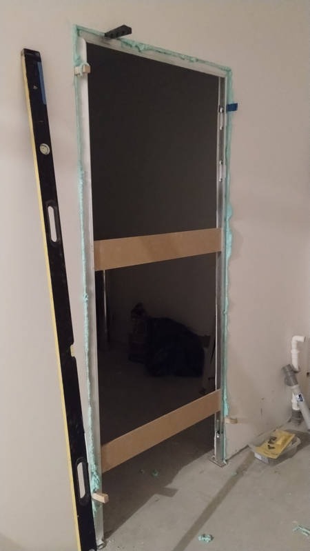 Montaż ościeżnicy drzwiowej z użyciem pianki montażowej i poziomicy, widoczne drewniane rozpórki stabilizujące