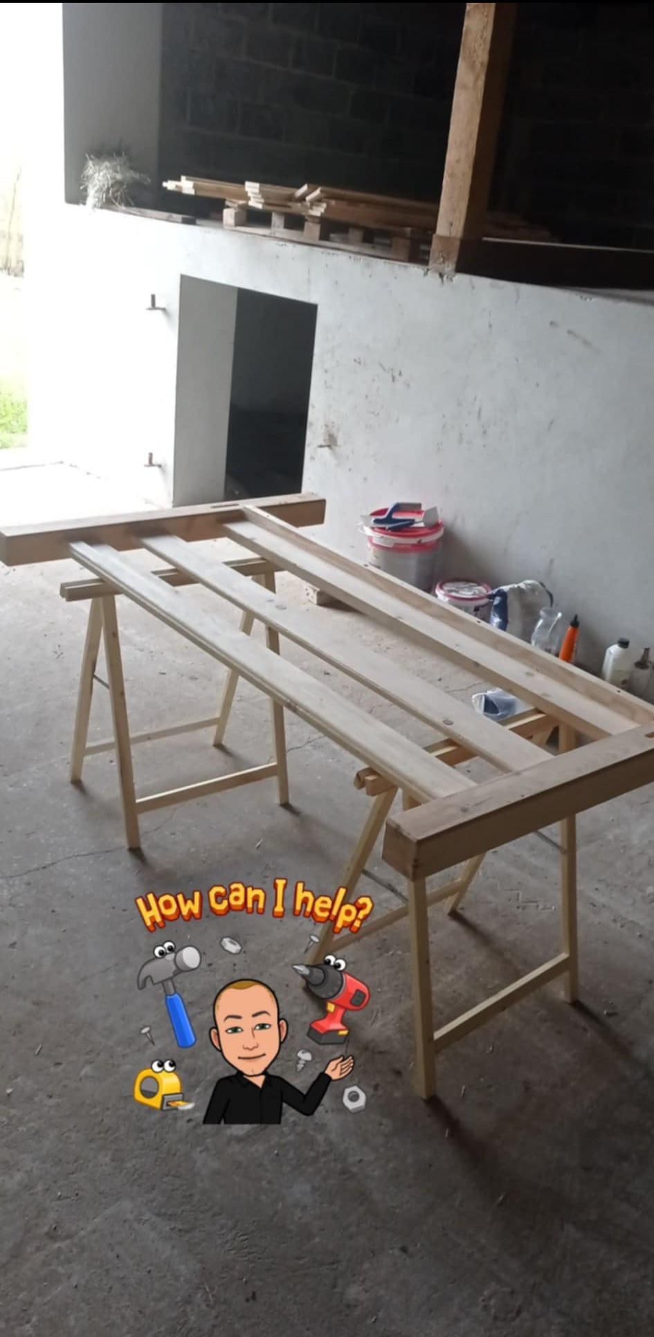 Drewniana konstrukcja ramy okiennej na kozłach w surowym wnętrzu. W tle widoczne narzędzia i materiały budowlane. Dodana grafika z postacią i tekstem 'How can I help?'.