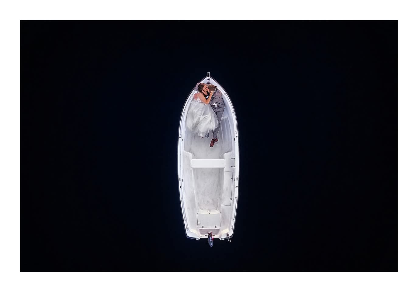 Para młoda w łodzi, pocałunek z lotu ptaka na tle ciemnej wody.