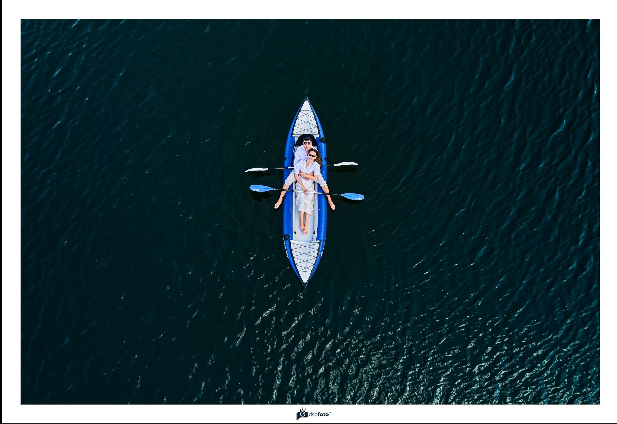 Para w okularach przeciwsłonecznych relaksuje się w niebieskim kajaku na ciemnej wodzie, widok z lotu ptaka.