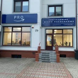 Fasada budynku biura rachunkowego z dwoma szyldami: 'PRO' z symbolem strzałki oraz 'CERTYFIKOWANE BIURO RACHUNKOWE' z adresem strony internetowej i numerem telefonu, widok z zewnątrz na wejście...