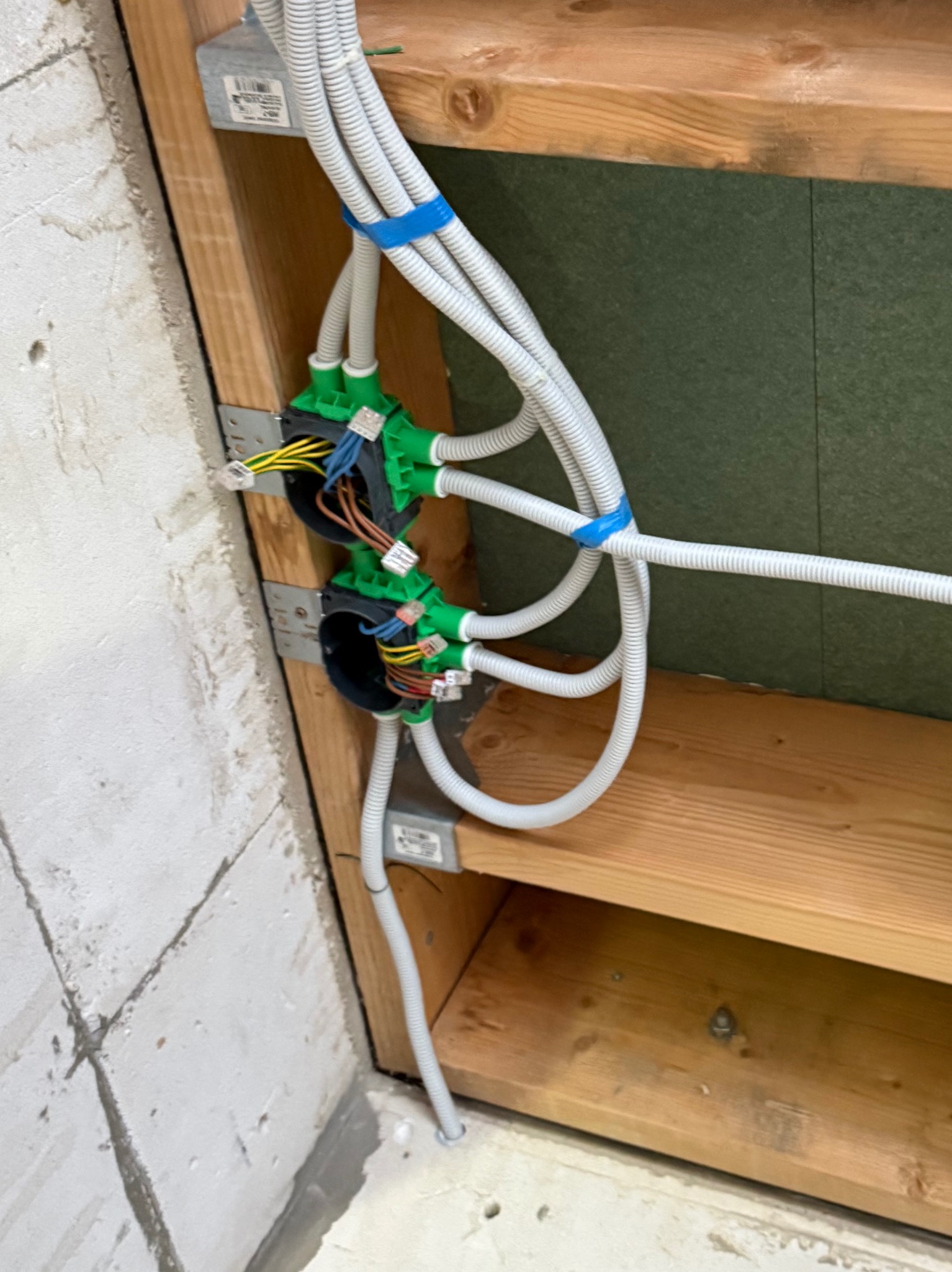 Wewnętrzna instalacja elektryczna w trakcie montażu: kable w peszlach, puszki instalacyjne z widocznymi przewodami, mocowane do drewnianej konstrukcji w surowym wnętrzu.