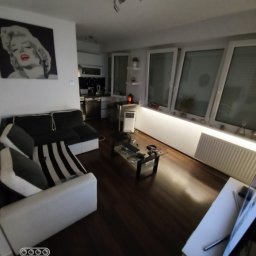 Budimar Bartosz Lewandowski - Salon z ciemną podłogą, jasnymi ścianami i oknami, meble w odcieniach bieli i czerni, obraz z Marilyn Monroe na ścianie.