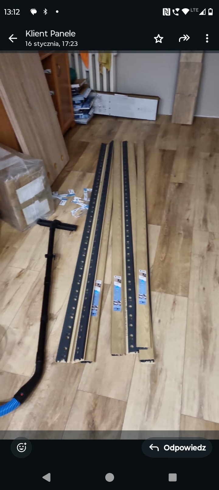 Przygotowane do montażu panele podłogowe z listwami przypodłogowymi i narzędziem do montażu na drewnopodobnej podłodze.