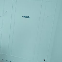 Rafał Aniszewski - Świeżo pomalowana, biała ściana z dekoracyjnymi panelami i przygotowanym gniazdkiem elektrycznym, widoczne drobne niedoskonałości malarskie przy podłodze.