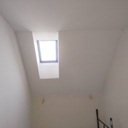 Rafał Aniszewski - Poddasze po remoncie z oknem dachowym; świeżo pomalowane ściany na biało, widoczne ślady po gładzi, fragment rusztowania w prawym dolnym rogu.