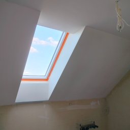 Rafał Aniszewski - Poddasze z oknem dachowym po remoncie: białe ściany i sufit, widoczne niebo. Częściowo wykończona ściana na dole. Wiszące kable elektryczne.