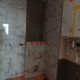 Rafał Aniszewski - Ściana łazienki z marmurowymi płytkami w trakcie montażu, widoczne krzyżyki dystansowe, instalacja wodna i gazowa. Częściowo wykończona ściana z zamontowanym geberitem.