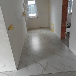 Rafał Aniszewski - Wykończone podłogi z białych płytek imitujących marmur w jasnym wnętrzu w trakcie prac wykończeniowych. Widoczne przygotowania do dalszych prac.