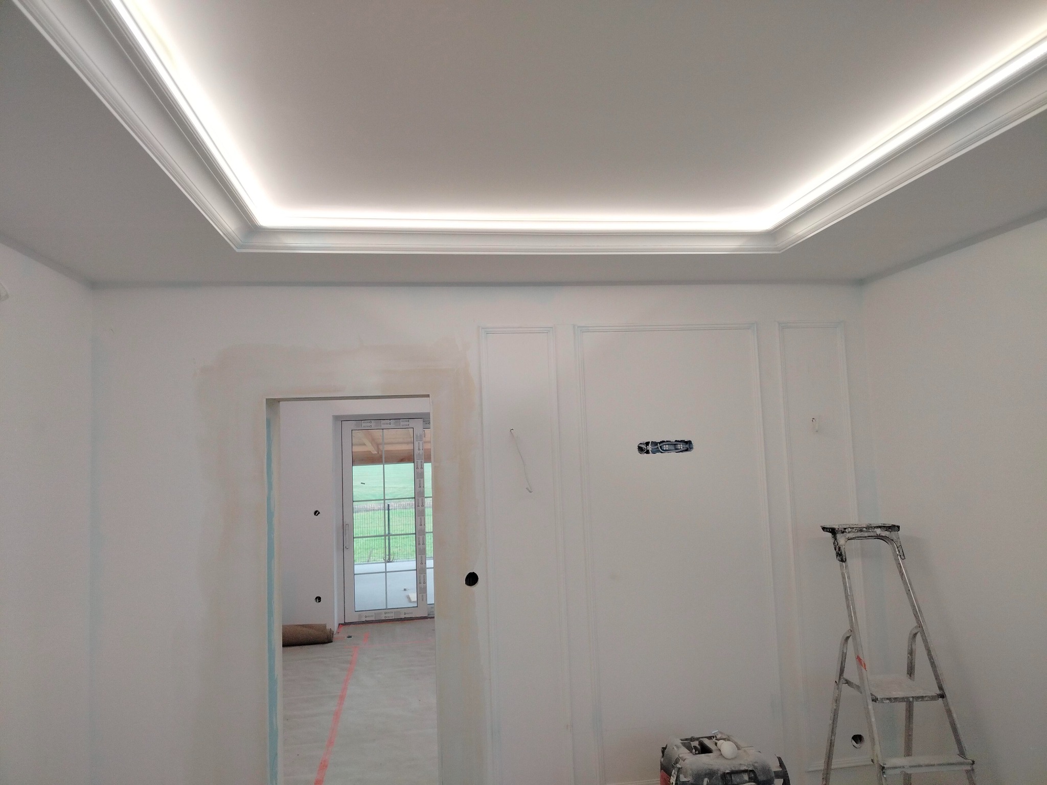 Pokój w trakcie prac wykończeniowych: ściany po szpachlowaniu, widoczna drabina malarska i listwa oświetleniowa pod sufitem.