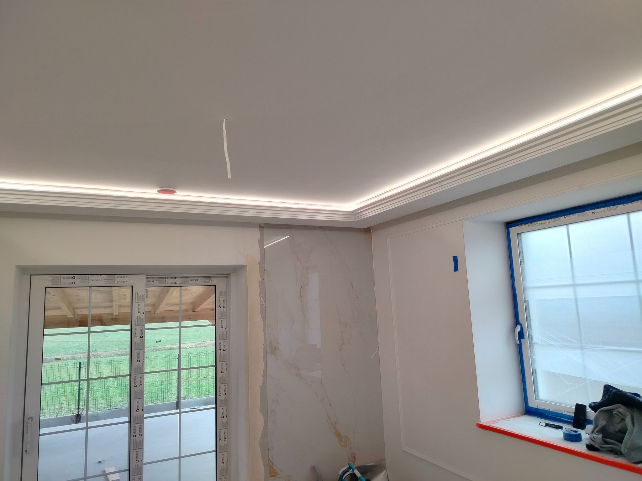Wykończone wnętrze w Siedlcach z podświetlanym sufitem, marmurową ścianą i dużym oknem, zabezpieczonym folią malarską.