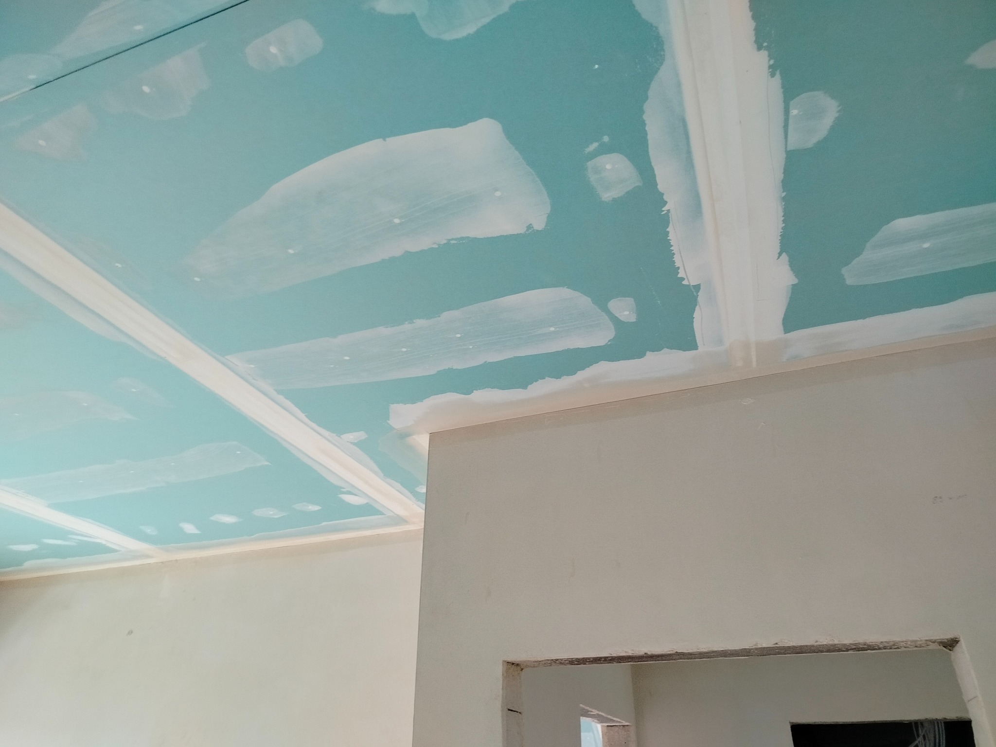 Niebieski sufit z płyt kartonowo-gipsowych w trakcie szpachlowania, widoczne łączenia i białe pasy szpachli. Ściany w jasnym odcieniu, fragment otworu drzwiowego.