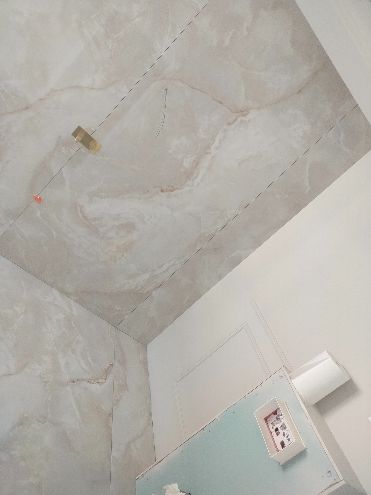 Wykończona łazienka z marmurową okładziną ścian i sufitu, widok z dołu. Widoczne elementy instalacji elektrycznej i fragment ściany z płyt gipsowo-kartonowych.