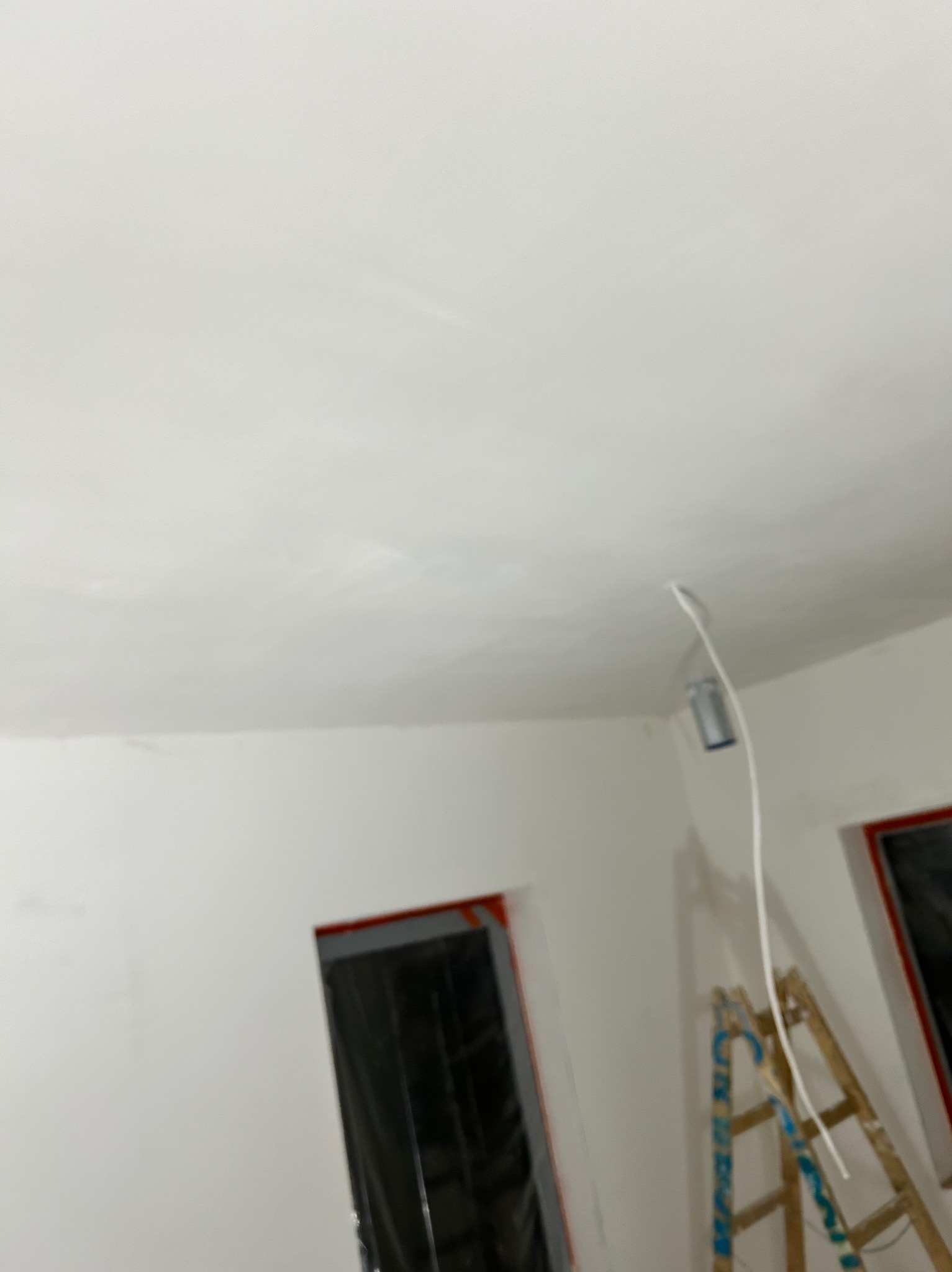 Wnętrze w trakcie remontu: świeżo wykończona, biała sufit z widocznymi śladami szpachlowania, drabina oparta o ścianę, okna zabezpieczone folią.