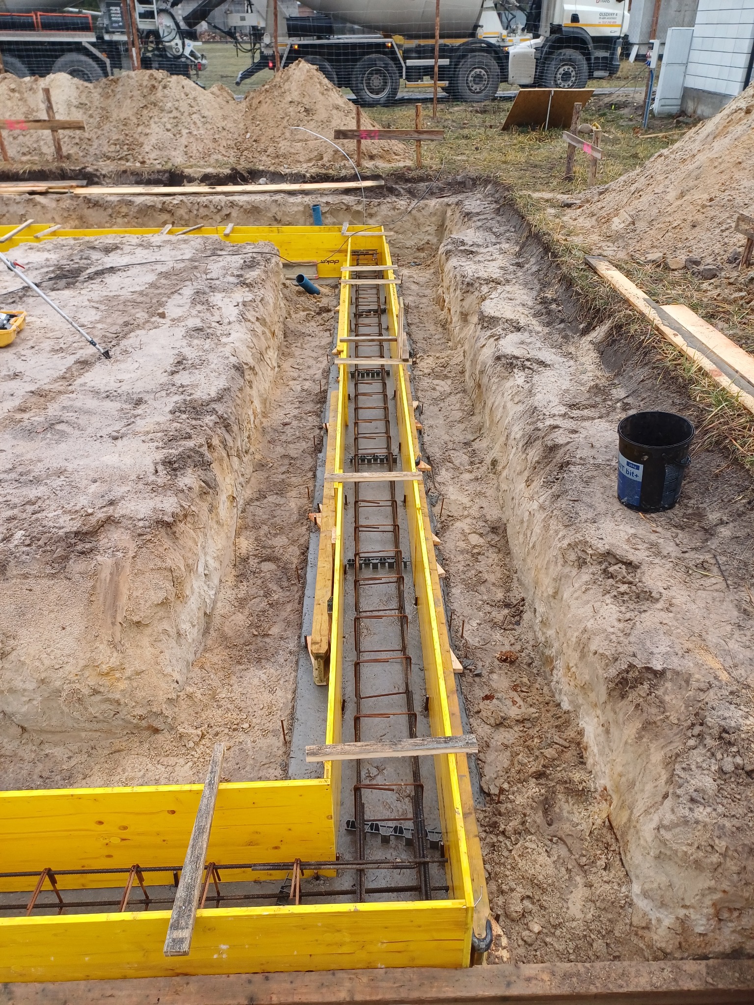 Przygotowanie szalunków i zbrojenia pod fundament w Trablice, widoczny betonowóz w tle.