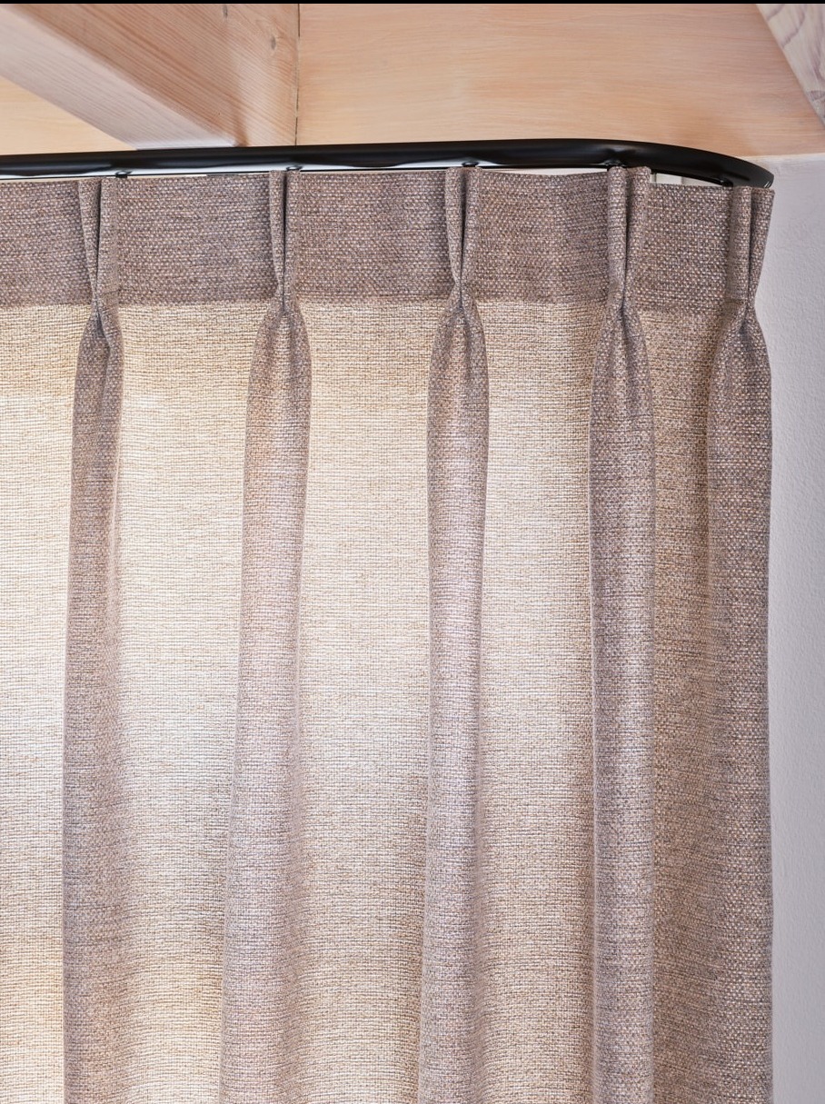 Beżowa zasłona z lnu, zawieszona na czarnym, zakrzywionym karniszu, z widocznym drewnianym elementem sufitu.
