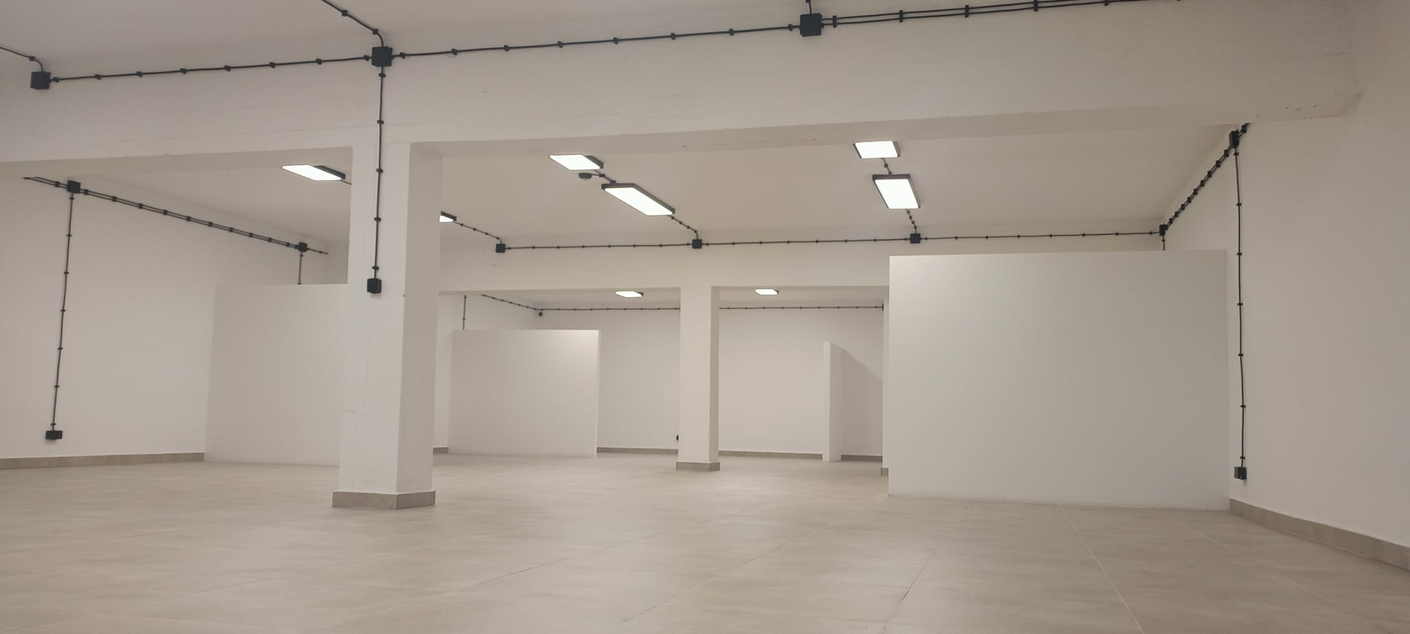 Wnętrze nowo wykończonego, pustego pomieszczenia z białymi ścianami, szarą podłogą i czarną instalacją elektryczną na suficie i ścianach.