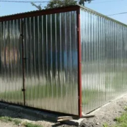 Gotowy, metalowy garaż z blachy trapezowej, z dwuskrzydłowymi drzwiami, na betonowej podmurówce, z brązowymi obramowaniami, widziany z boku w słoneczny dzień.